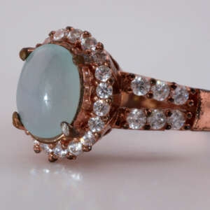 Three-quarter view of Type-A jadeite jade oval ring showing rose-gold setting and sparkling round accent stones, size 7.5