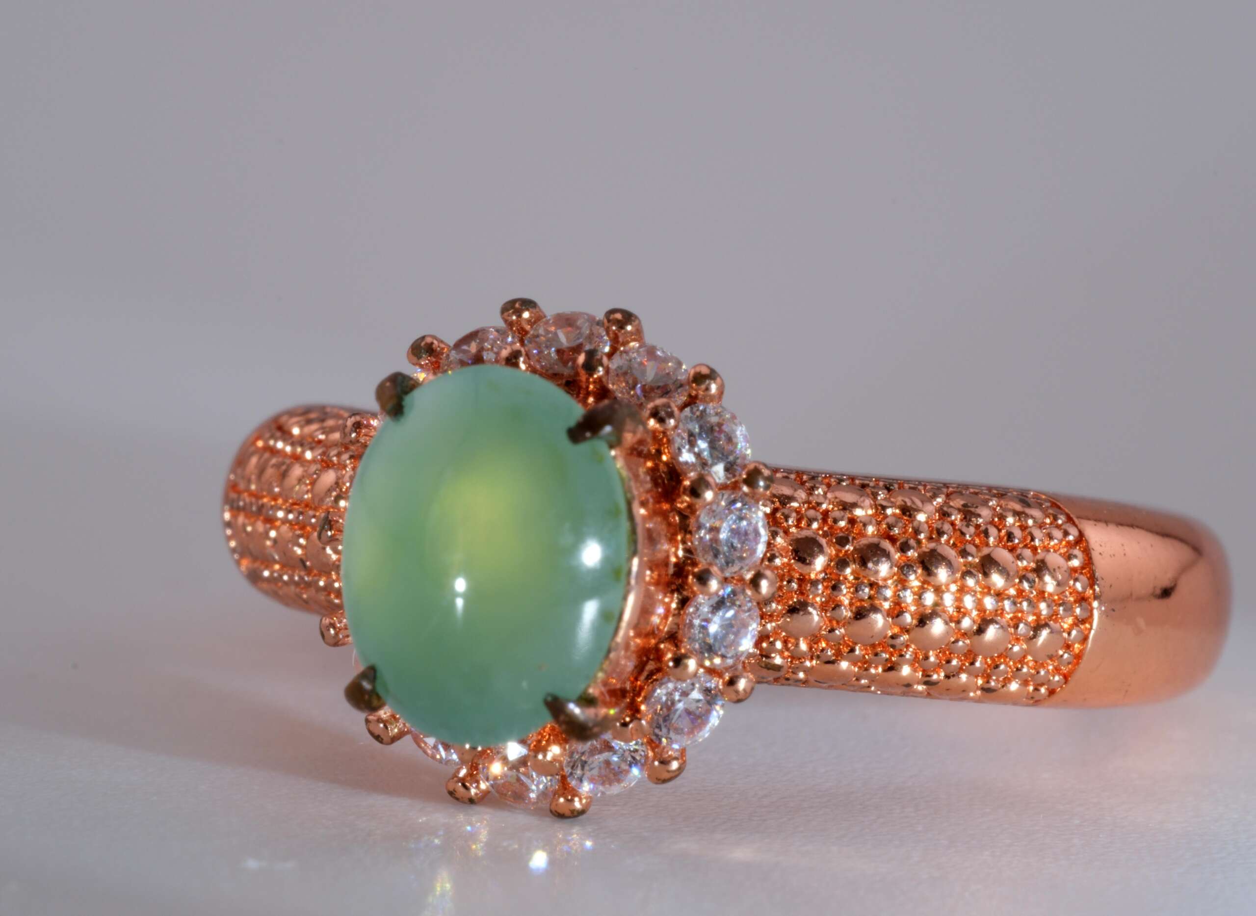 Three-quarter angle of Burmese jadeite ring showing light apple-green oval cabochon and pavé halo, size 8