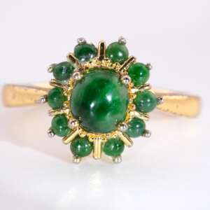 A gold-plated ring featuring a glossy green jadeite cabochon at the center, surrounded by a circular halo of small round jade cabs in a floral arrangement.